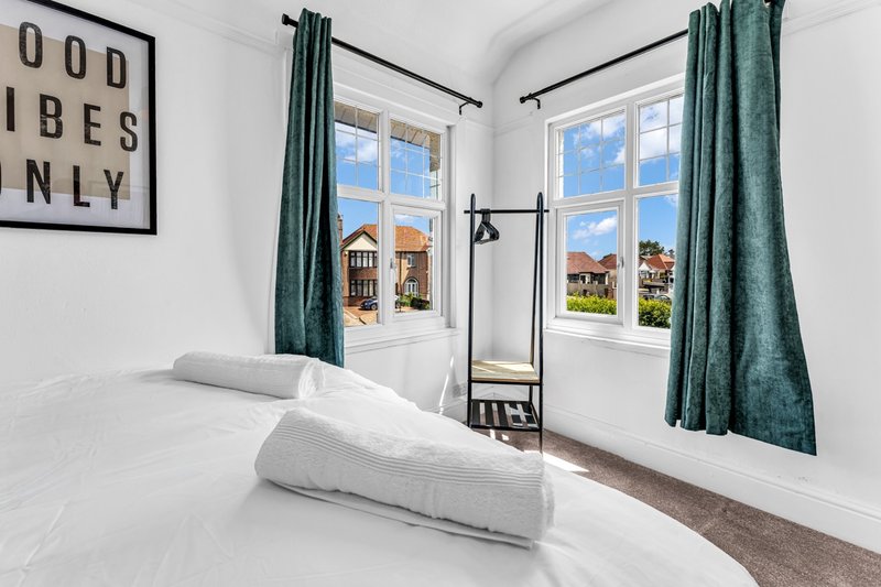 Bright bedroom with double bed, green curtains, large windows overlooking garden, wall art