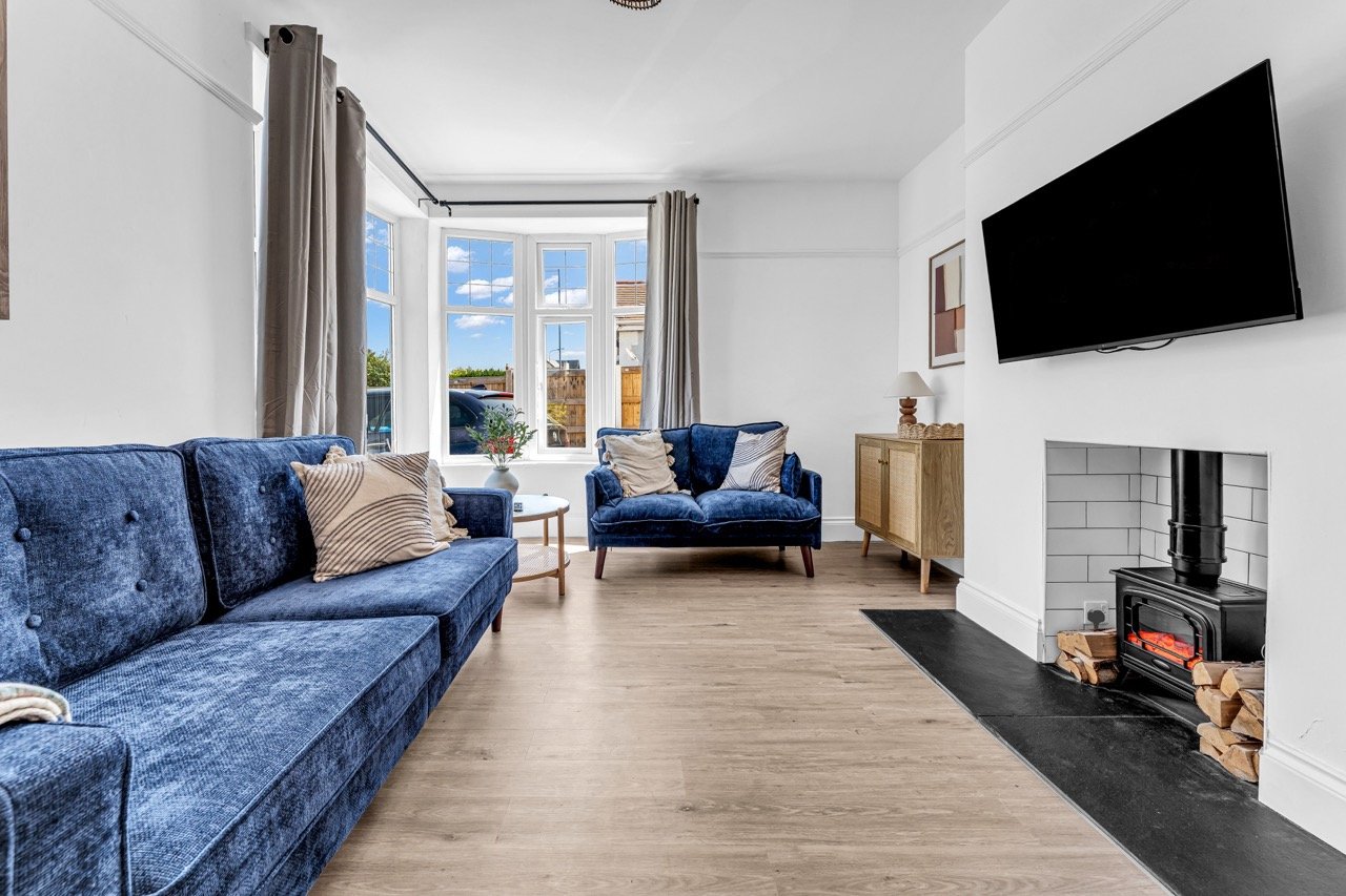 Spacious modern living room with blue velvet sofas, fireplace, wall-mounted TV, and large windows