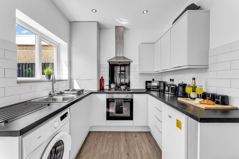 Modern white kitchen with black countertops, stove, sink, and appliances