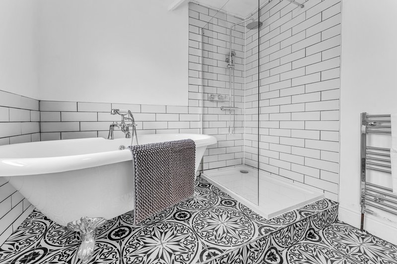 Modern bathroom with freestanding white bathtub, subway tile walls, patterned floor tiles, and shower area
