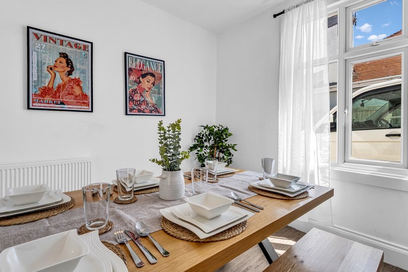 Dining room with wooden table, place settings, water glasses, and framed vintage posters on wall
