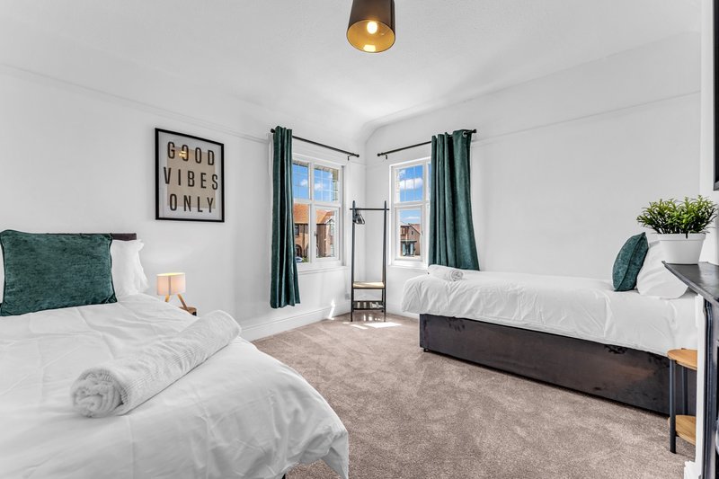 Bright modern bedroom with two single beds, white bedding, green cushions, and double doors to balcony