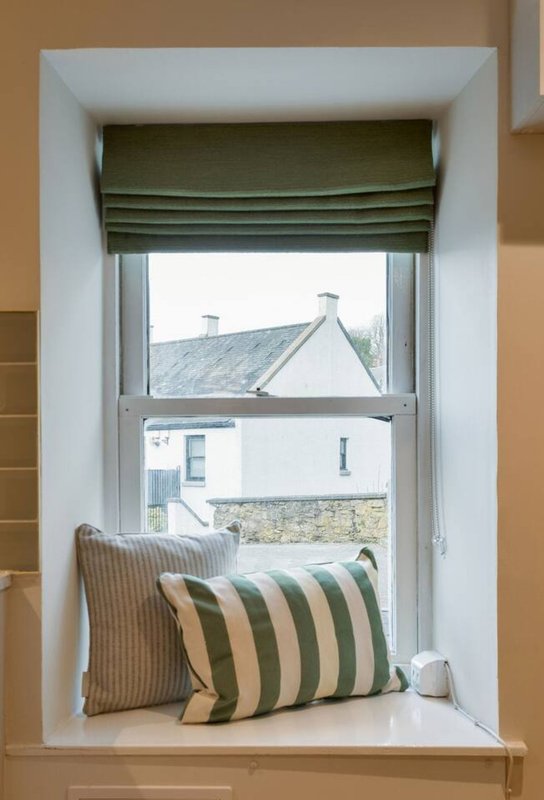 Window seat with striped cushions and green roman blind, overlooking stone buildings