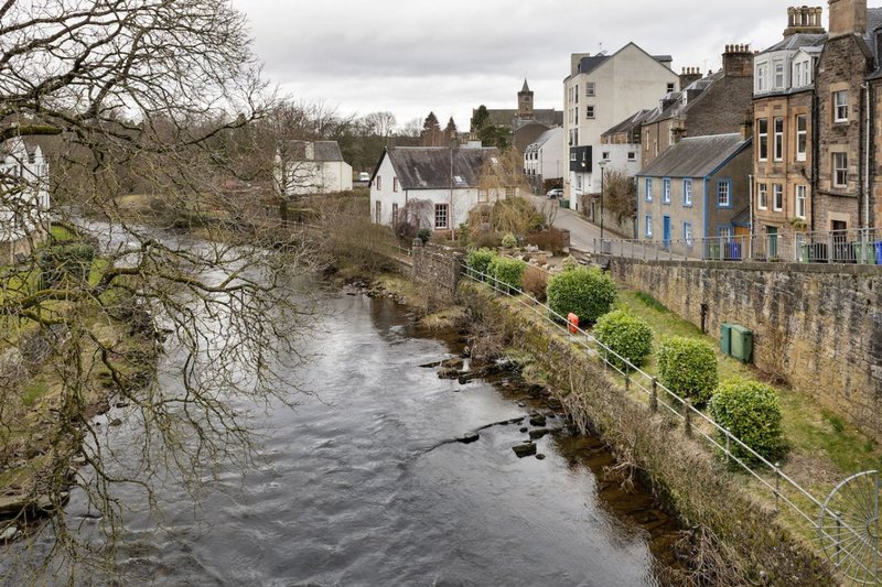 River view with stone townhouses, bare tree branches, and overcast sky