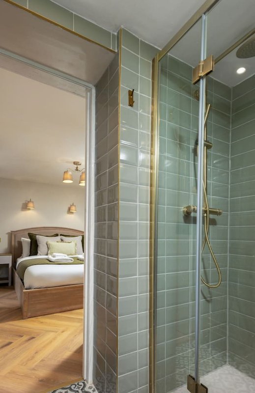 Ensuite bathroom with walk-in shower, green tile walls, brass fixtures and adjacent bedroom view