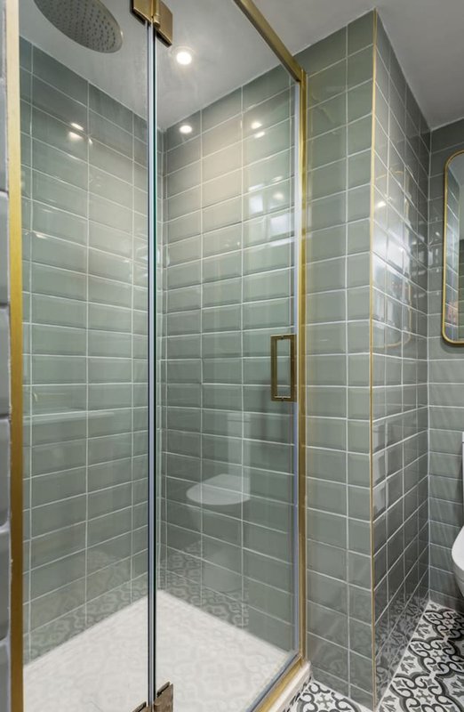 Modern bathroom with large walk-in shower, green tile walls, brass frame and rainfall showerhead