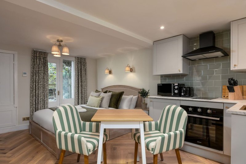 Open-plan studio with kitchenette, dining table, striped chairs and bed seating area