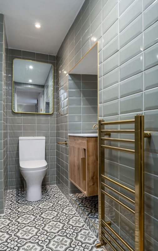 Modern bathroom with toilet, sink, mirror, heated towel rack and grey tile walls