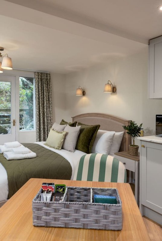 Modern bedroom with double bed, olive bedding, pendant lights, wooden desk and glass doors to garden