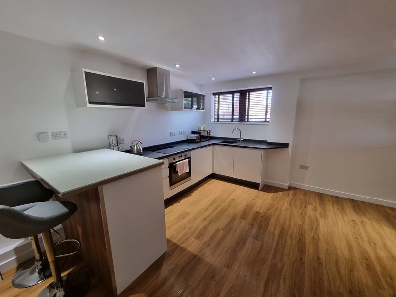 Modern kitchen with white cabinetry, black worktops, island seating, and wooden flooring