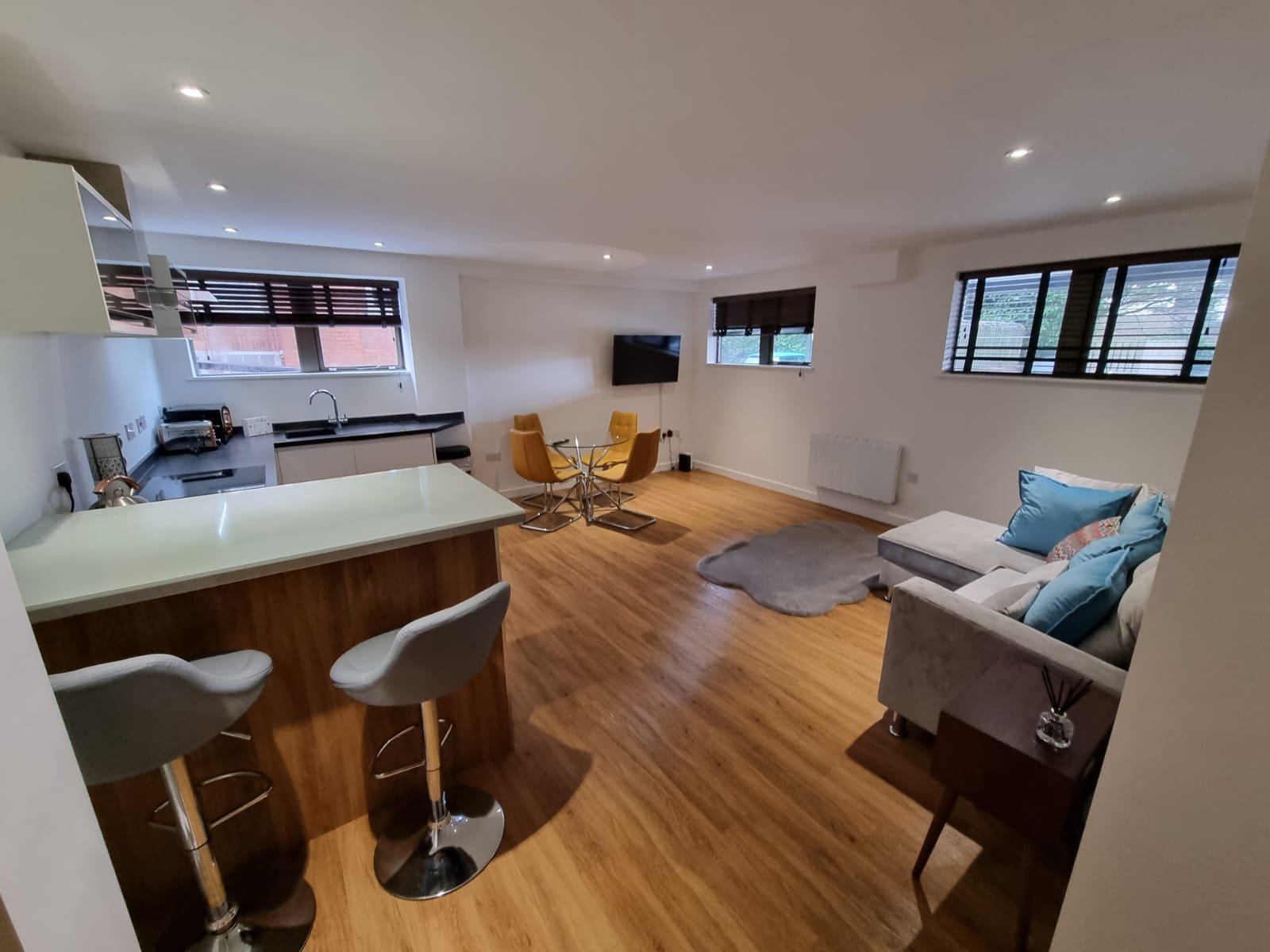 Open-plan studio with kitchen counter, bar seating, sofa and wooden flooring throughout