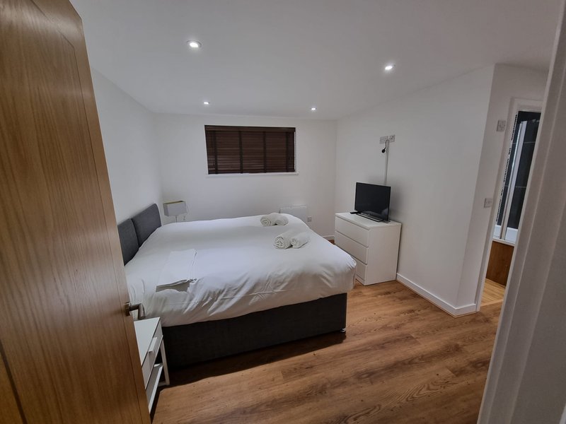 Bedroom with double bed, wooden flooring, TV stand, and white walls with recessed lighting