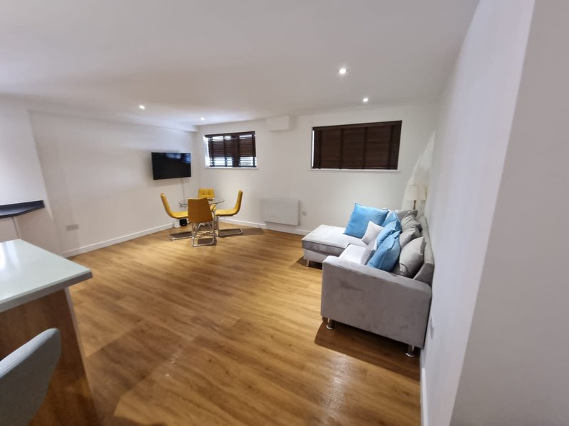 Open-plan living room with wooden floors, gray sofa, dining table and wall-mounted TV