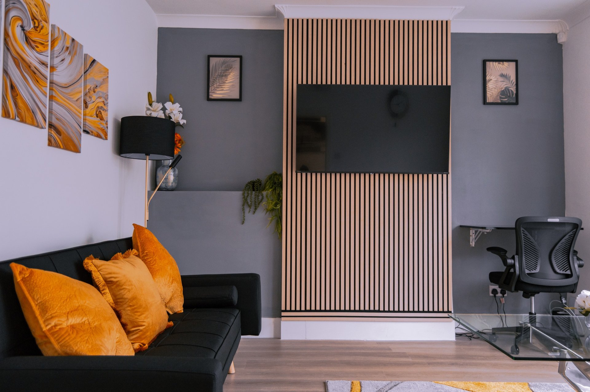 Modern living room with black sofa, orange cushions, wall-mounted TV, and wooden accent paneling