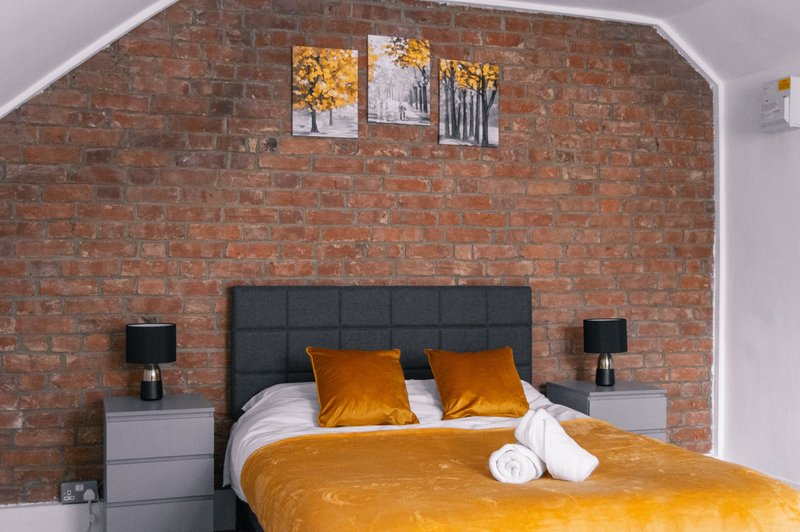 Bedroom with exposed brick wall, double bed, gold bedding, and framed wall art