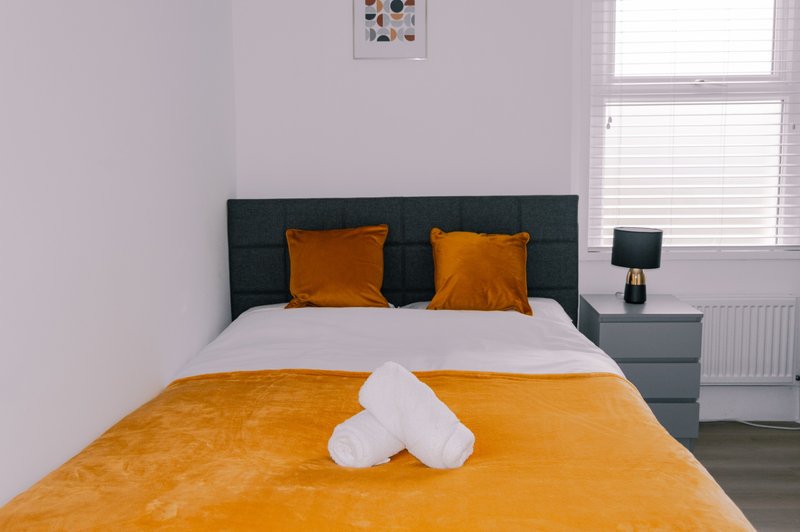 Modern bedroom with orange bedding, dark headboard, two pillows and white towels on bed