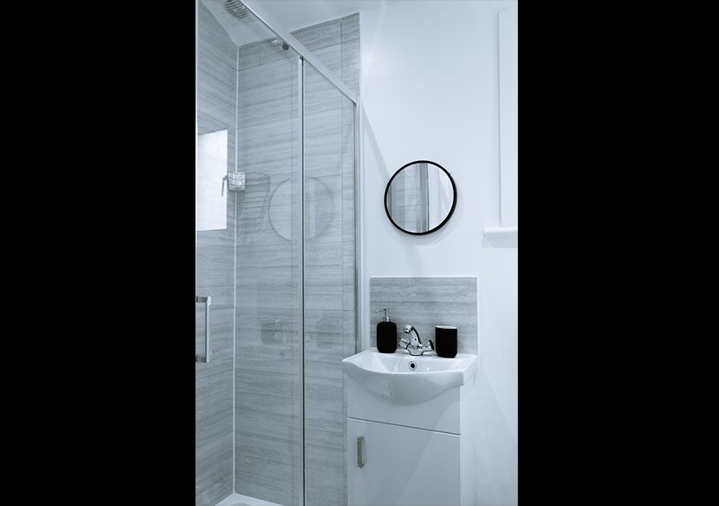 Modern bathroom with glass shower enclosure, white sink vanity and round mirror