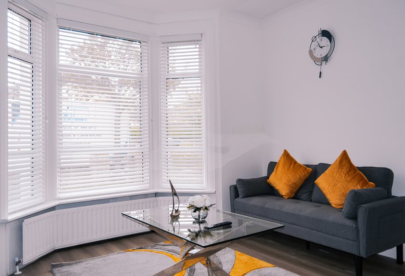Modern living room with dark sofa, bay windows with shutters, wall clock and yellow accents