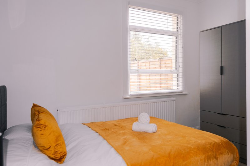 Bedroom with single bed, yellow cushion, orange bedding, white pillows and dark wardrobe