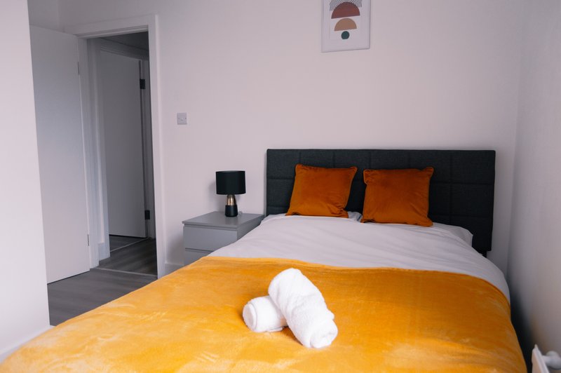 Modern bedroom with double bed, orange bedding, black headboard, and en-suite bathroom entrance