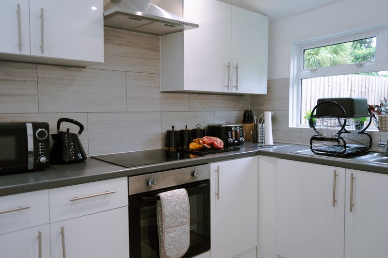 Modern white kitchen with black countertops, stainless steel oven, and window overlooking garden