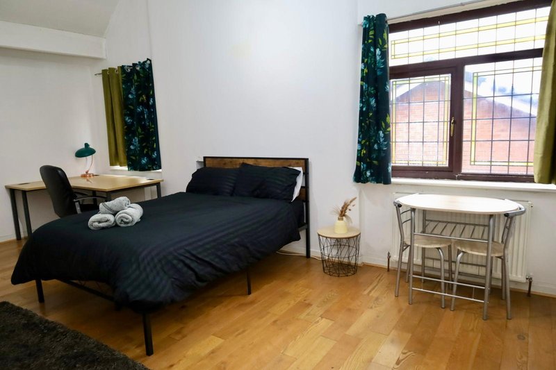 Bedroom with black bed, wooden desk, chair, and hardwood flooring with window