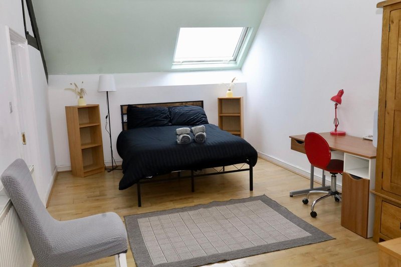 Attic bedroom with skylight, double bed, wooden furniture, desk chair and gray armchair
