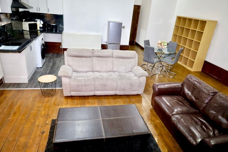 Open-plan living room with beige sofa, brown leather armchair, wooden flooring and kitchen area