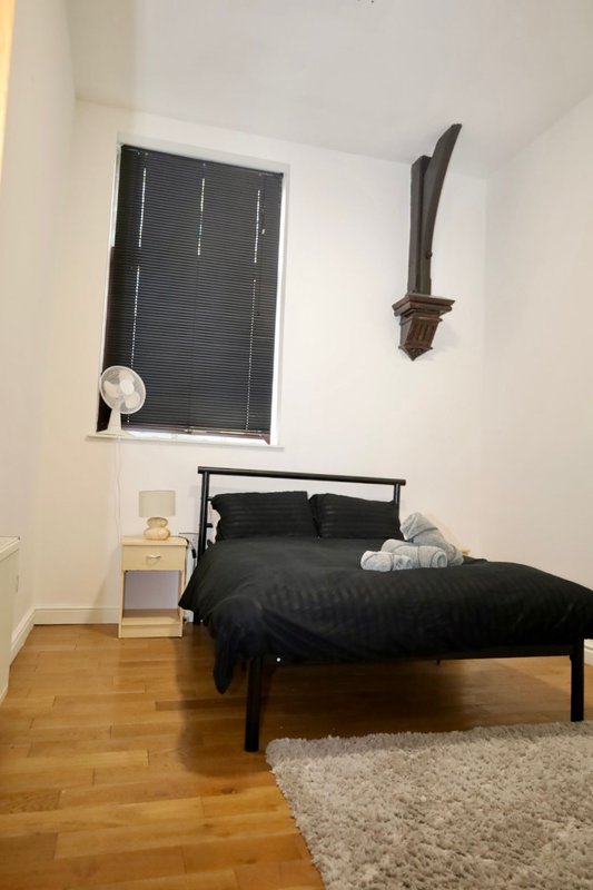Bedroom with black metal bed frame, dark bedding, wooden floor, window with blinds