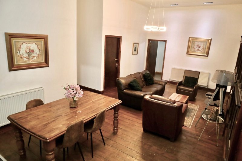 Open-plan living and dining area with wooden table, brown leather sofa, framed wall art and pendant lighting