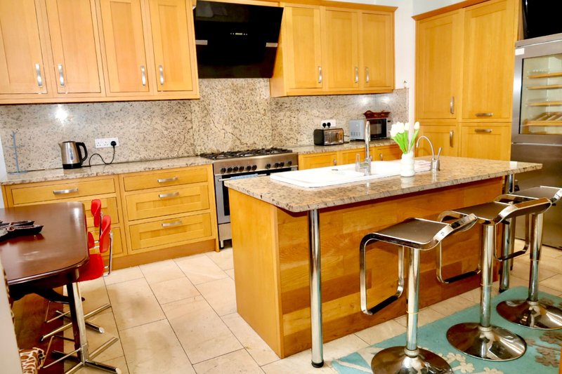 Modern kitchen with golden wood cabinets, granite countertops, island seating, and stainless steel appliances