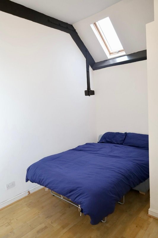 Modern bedroom with blue bedding, wooden floor, skylight and black exposed beams