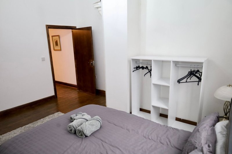 Bedroom with double bed, white wardrobe with hangers, wooden door and hardwood floor