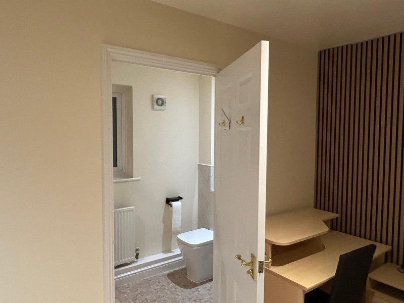 Bathroom with toilet, sink and tiled walls, viewed from bedroom with wooden platform bed