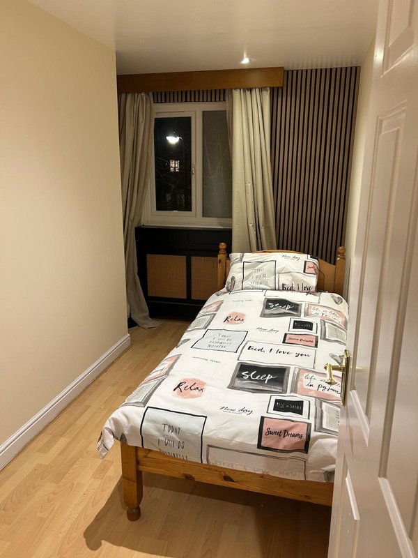 Single bedroom with wooden bed, patterned bedding, window with curtains and desk