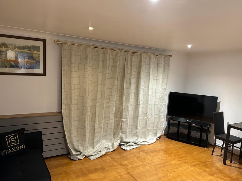 Living room with cream curtains, wooden floor, TV stand and framed wall art