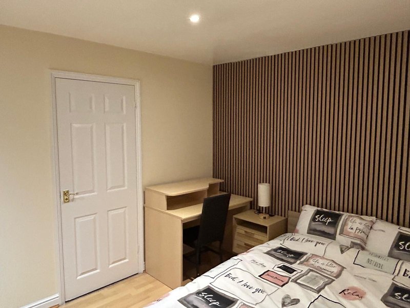 Bedroom with desk, chair, bed with patterned bedding, white door and vertical striped curtains