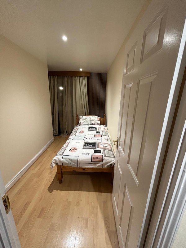 Narrow bedroom with single bed, wooden floor, white wardrobe doors and curtains