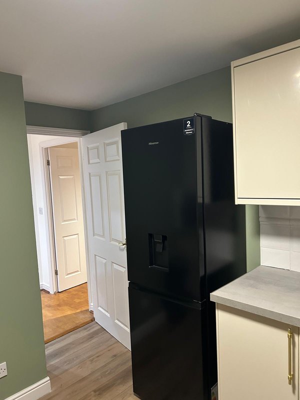Kitchen with black refrigerator, cream cabinetry, green walls, and wooden flooring
