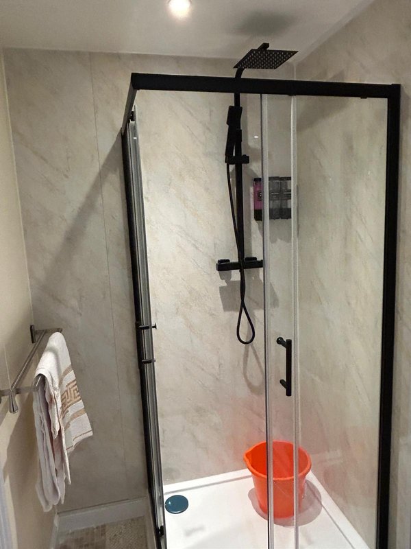 Modern bathroom shower enclosure with black frame, marble tiles, rainfall showerhead and orange bucket