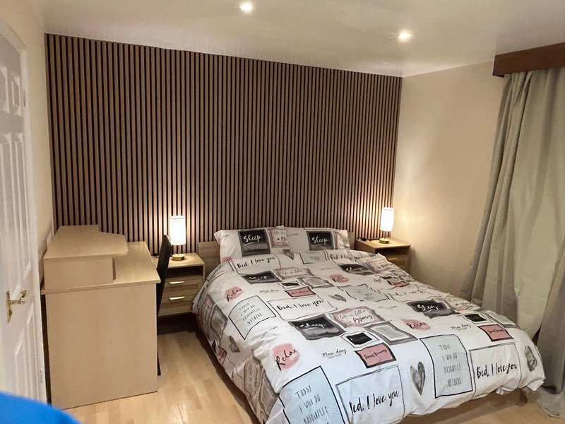 Bedroom with double bed, bedside tables, lamps, vertical wall paneling, and cream armchair