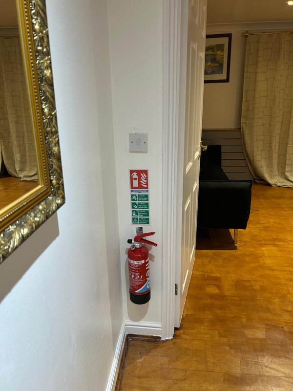 Hallway interior with white wall, framed mirror, fire extinguisher, and wooden flooring