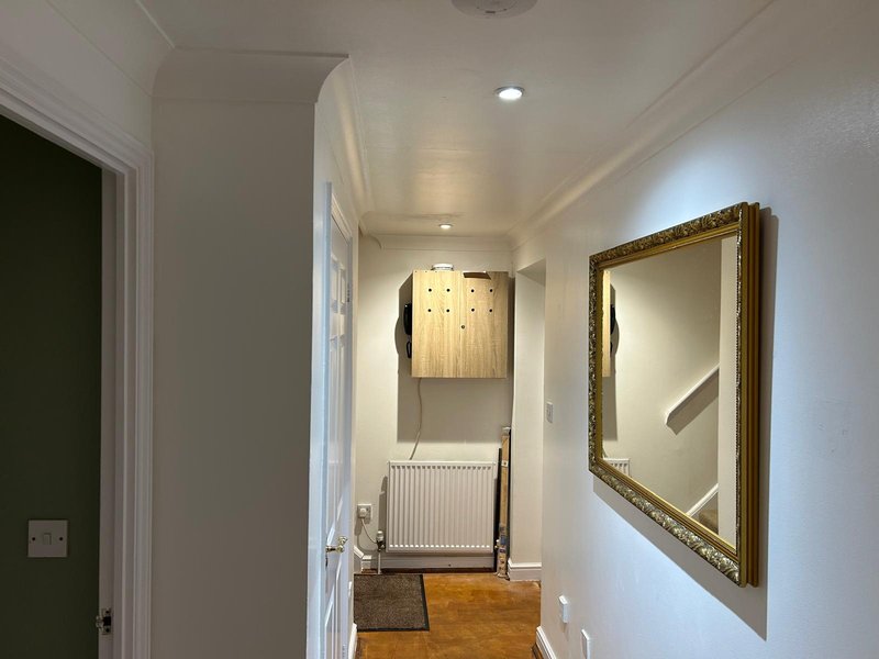 Bright hallway with white walls, framed mirror, radiator and wooden flooring