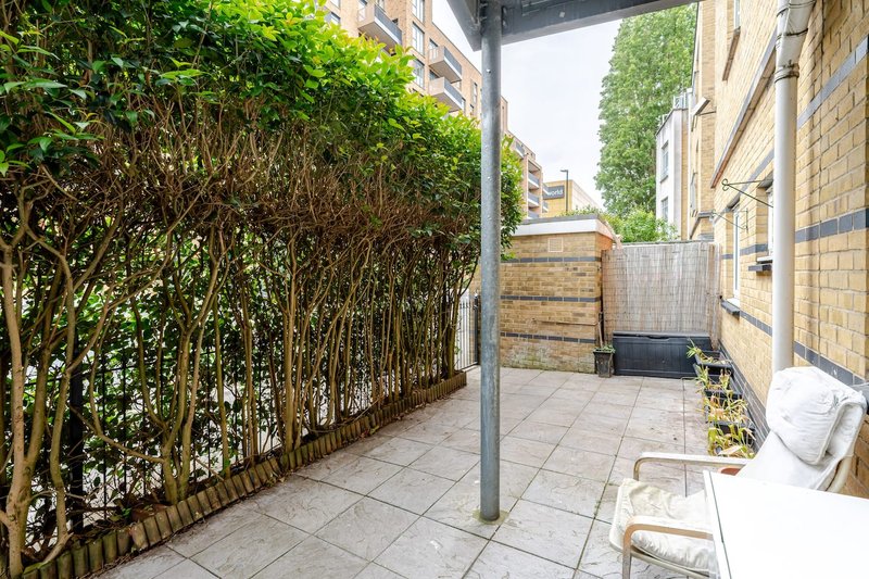 Paved courtyard with climbing ivy, metal post, white chair and potted plants