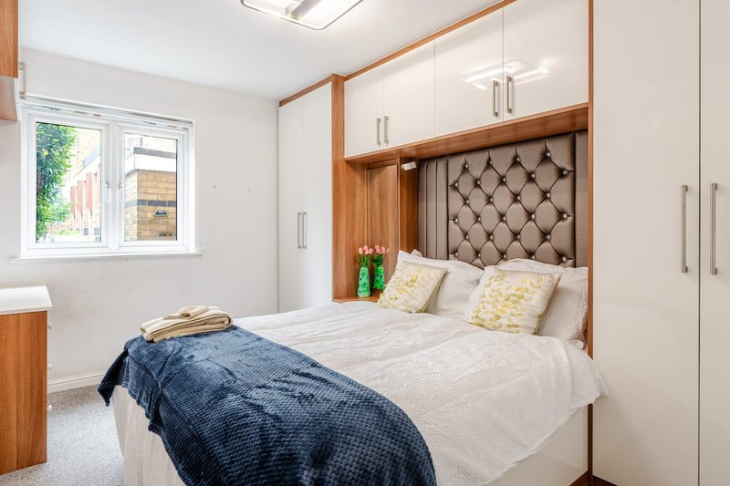 Modern bedroom with double bed, built-in wooden wardrobes, upholstered headboard and natural light from window