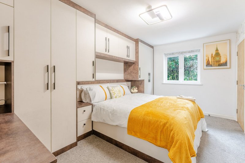 Modern bedroom with built-in storage, double bed, yellow throw, and window with garden view