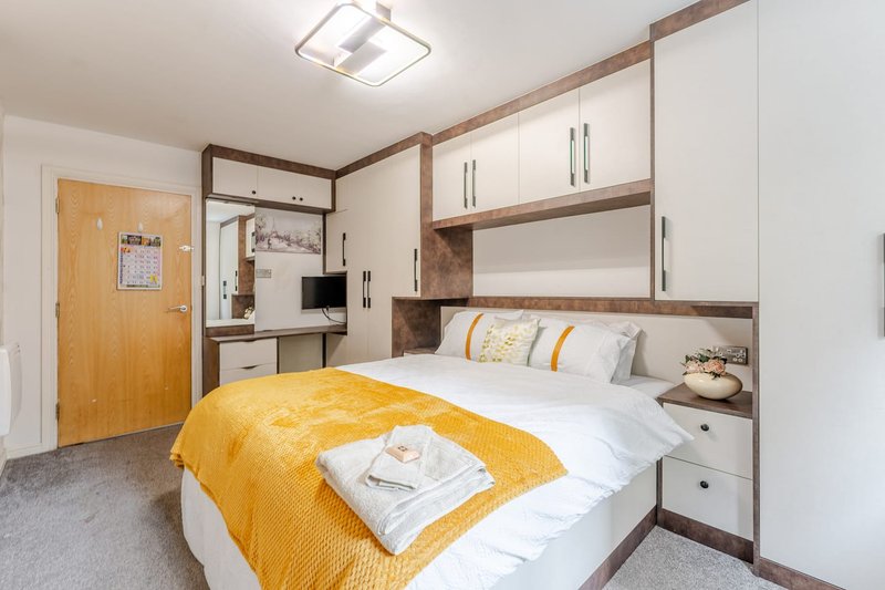 Modern bedroom with double bed, yellow throw, built-in storage, and wooden door