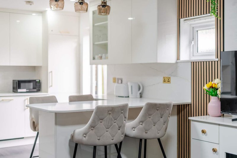 Modern kitchen with white cabinetry, island, gray upholstered chairs, and open-plan living area