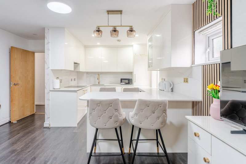 Modern kitchen with white cabinetry, island seating, pendant lighting and wooden entrance door