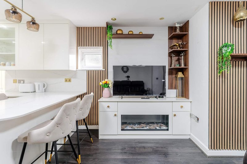 Modern open-plan kitchen and living area with white cabinetry, wooden slat wall paneling, and fireplace